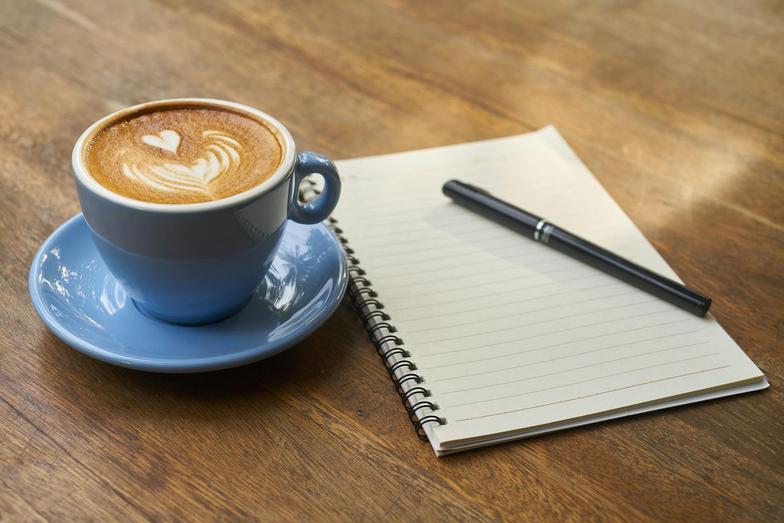 温かい光の差す机に置かれたコーヒーと開いたノート